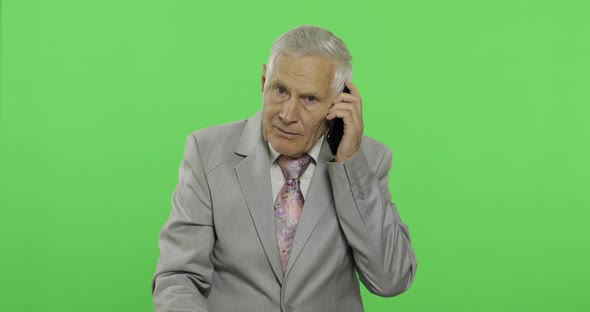 Handsome Elderly Businessman Talks on a Smartphone. Old Man in Suit