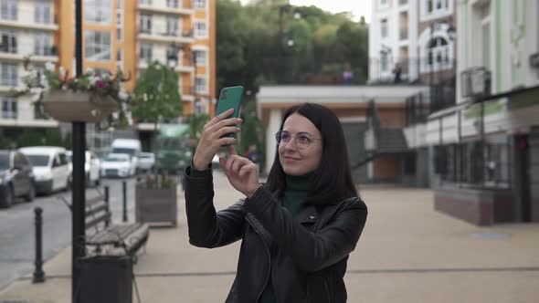 Young happy girl photographs a beautiful city on a smartphone.