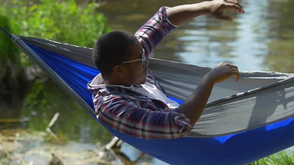 A man resting in a hammock near a mountain lake.