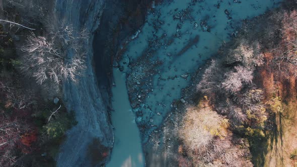 Aerial view above a blue river in middle of leafless, foliage forest, sunny, fall day - rising, top