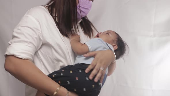 Mother Wearing Mask Carrying And Putting The Baby Boy To Sleep. - close up