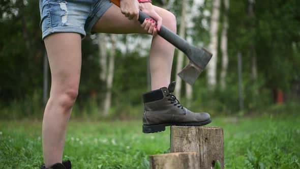 Young woman with red nails takes an ax and is about to chop wood