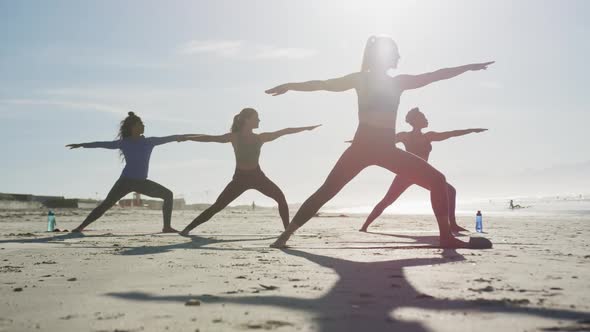 Group of diverse female friends practicing yoga at the beach