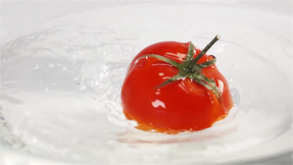 One Red Ripe Tomato with Green Leaves Falls Under Water