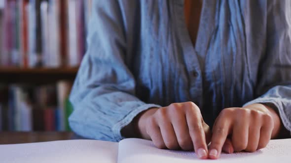 Asian female student wearing a blue hijab sitting and reading a braille book with closed eyes