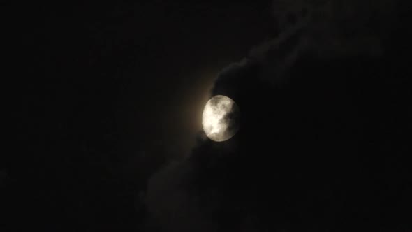 Timelapse of the full moon rises from behind the clouds. During the shot there are clouds that cross
