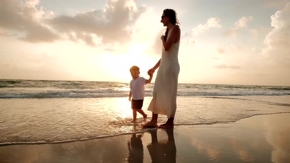 Mother and Son Walk Together on the Beach at Sunset