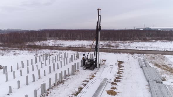 Aerial drone view of a pile bore machine and worker at winter construction site 20