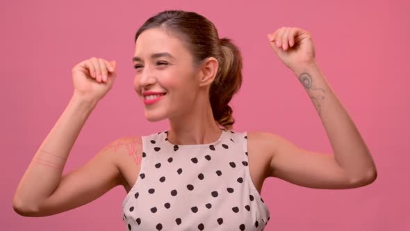 Happy Young Caucasian Woman Dancing in a Good Mood on a Pink Background.