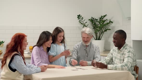 Cheerful Multiethnic Family of Different Age Generations Playing Cards at Home Sitting at the Table