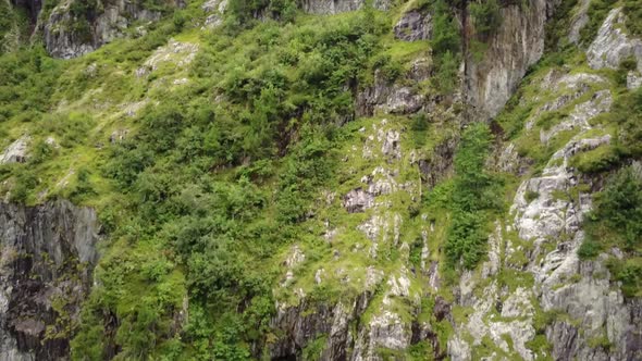 A drone flies next to a green and rocky facade in the swiss alps. aerial shot
