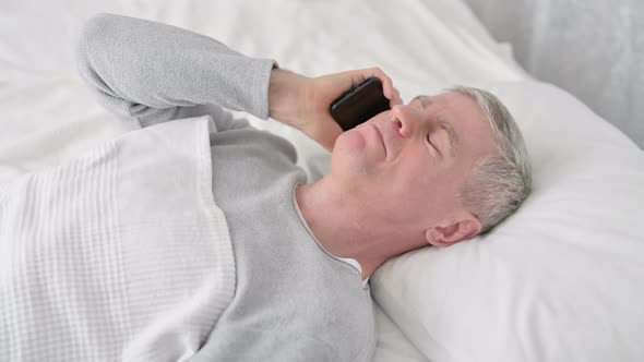 Positive Old Man Talking on Smartphone in Bed