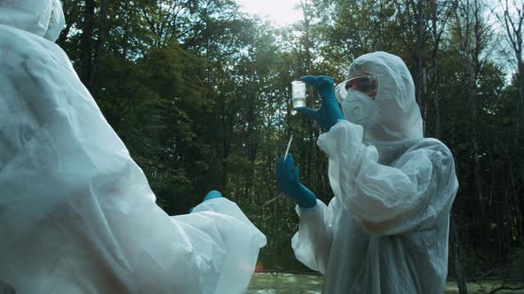 Chemists in Ppe Looking at Water Analysis From Swamp Using Flask and Pipette Wearing Protective Suit