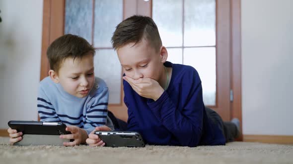 Two brothers involved in playing games on the digital gadgets at home.