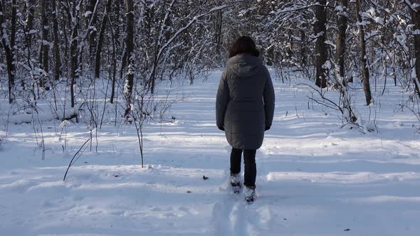 A woman in a gray jacket walks through the winter forest, park