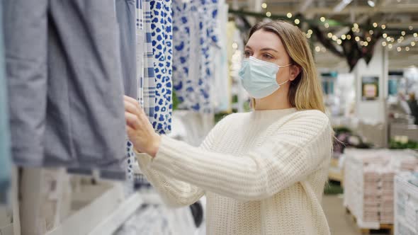 Woman in a Protective Mask Closeup in the Store Chooses Home Textiles Bed Linen