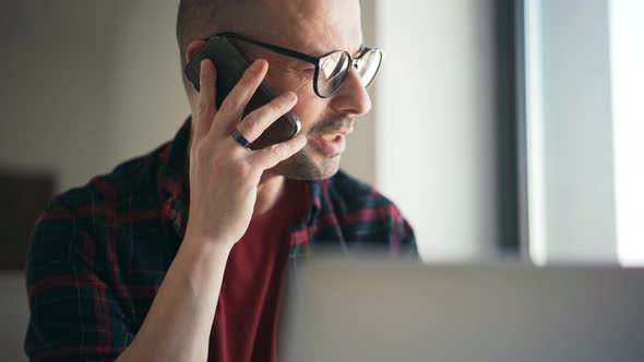 A Handsome Serious Man Is Talking on the Phone While Working on a Laptop at Home