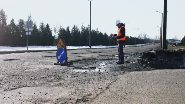 Engineer or Builder Looks, Inspects the Road Pits and Writes Notes To Tablet, Sign of Repair Work Is