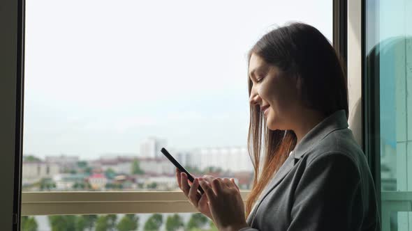 Woman in Business Suit Typing on the Phone By the Open Window on a Sunny Day