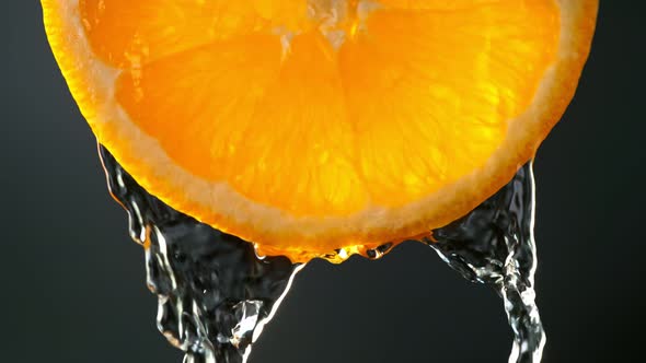 Super Slow Motion Macro Shot of Flowing Water From Fresh Orange Slice on Black at 1000Fps