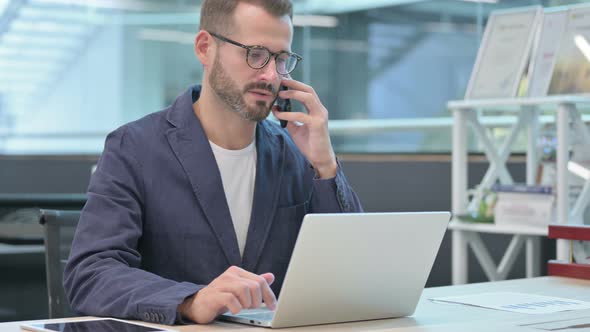 Middle Aged Businessman Using Smartphone While Working on Laptop