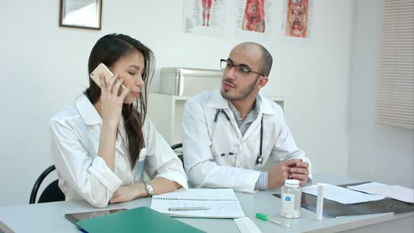 Female Doctor Talking on the Phone Asking Her Male Coworker for Advice