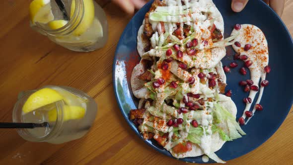 Top View of Hand Placing Dark Blue Plate with Tacos on Wooden Table. Two Jars of Lemonade. Clean