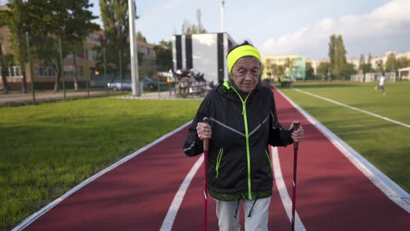 Active Elderly Caucasian Elderly Women of 90 Years Practice Nordic Walking with Ski Poles on a Track