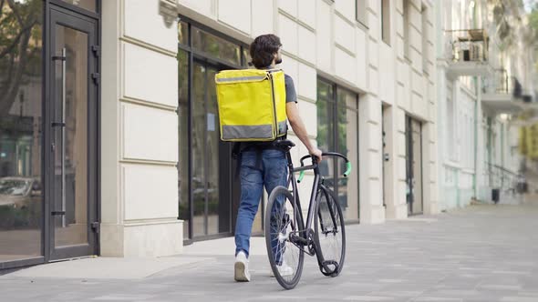 Delivery Man Walking with Bike and Yellow Bag Rear View