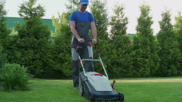 Young Gardener in Overalls Uses a Lawn Mower on the Plot
