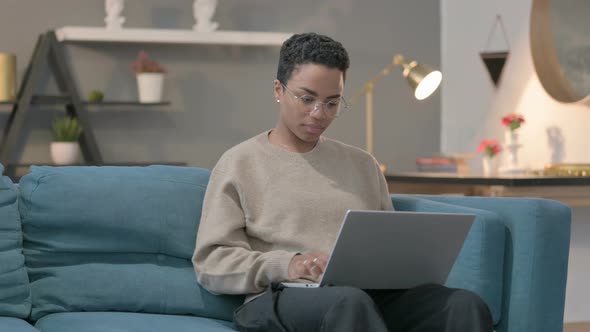 African Woman with Laptop Reacting to Loss on Sofa