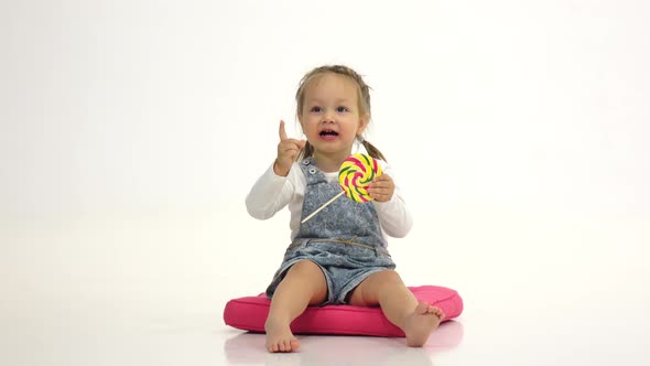 Little Girl Is Holding a Sweet Candy in Her Hands and Licks It. White Background