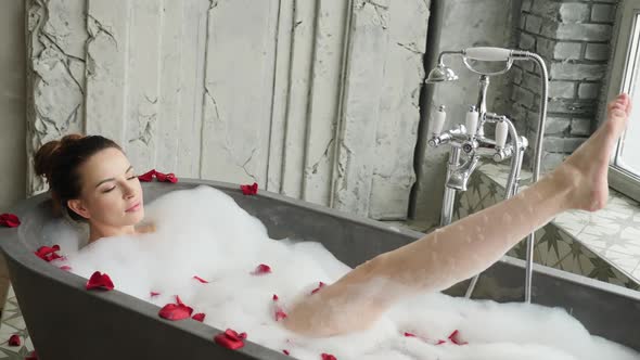 Girl Lies in a Large Stone Bath in Foam