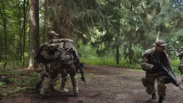 Military Squad Covering Injured Soldier to Evacuation Point in Forest alt
