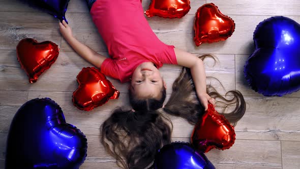 Cute girl lying on floor with balloons. Top creative view of little girl on floor with balloons 