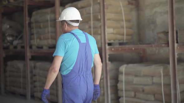 Camera Follows Confident Caucasian Man Walking on Manufacturing Site Storage Facilities. Adult Male