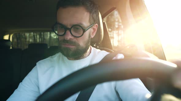 Man in Glasses is Parked in a Car in a Parking Lot Outdoors at Sunset