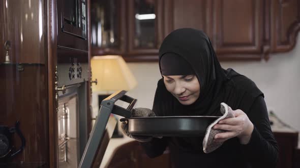 Portrait of Smiling Muslim Woman in Black Traditional Dress Smelling Baked Foods. Modern Eastern