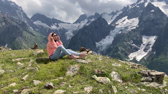 Young Woman Sitting on Rock and Looking at Mountain Landscape