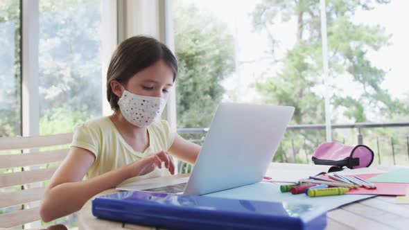 Girl wearing face mask using laptop at home