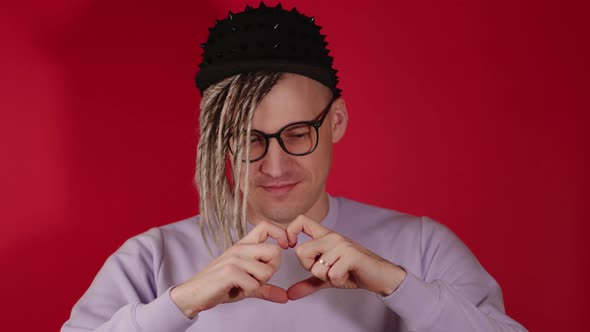 Young Handsome Stylish Man in Glasses with Blonde Dreadlocks Showing Heart with Hands