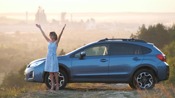 Young Female Driver Resting Near Her Car Raising Up Her Hands on Warm Summer Evening