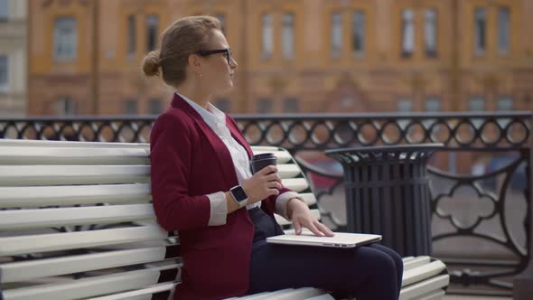 Side View of Successful Lady Entrepreneur Closing Laptop and Enjoying Coffee Relaxing on Bench