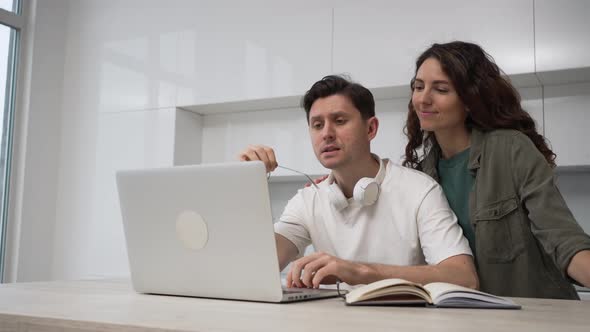 Freelance Man with Glasses Works at Home on a Laptop His Wife Comes Up and Encourages Him to Work