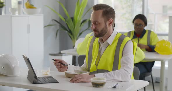 Foreman in Reflective Vest Having Video Chat While Eating Lunch in Canteen