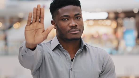 Closeup of Young Serious Confident African American Man Looking at Camera Puts Forward Palm Showing