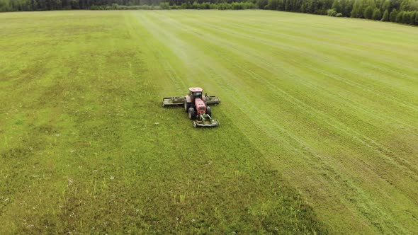 Farmer on a Red Tractor with a Combined Mounted Mower with Disc Rotary Knives Mows Grass Into Silage