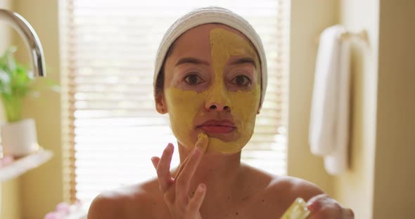 Portrait of biracial woman looking into mirror and applying face mask