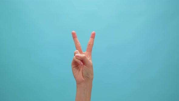 Woman raising two fingers up on hand on the blue background. Concept victory symbol.