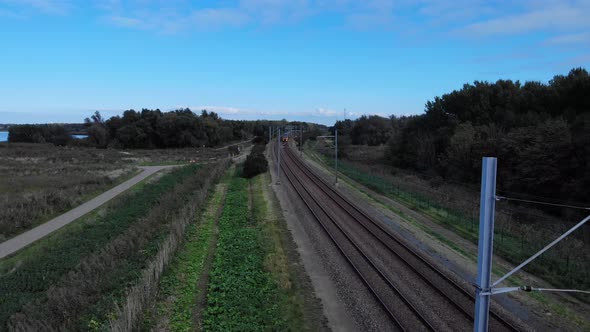 Dutch train is driving away from the drone on a railway track true the dutch nature on a sunny blue